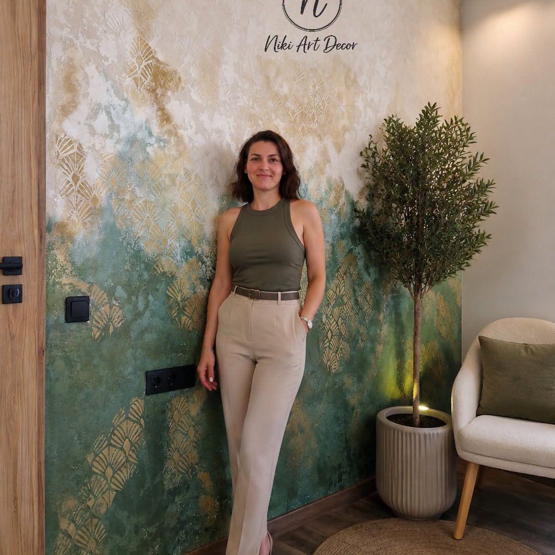 Niki, a Niki Art Decor alkotója egy zöld és arany dekorfal előtt